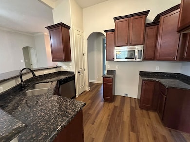 Kitchen featuring stainless steel appliances, arched walkways, dark stone countertops, dark wood finished floors, and ornamental molding