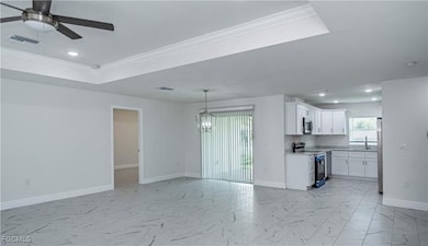 Unfurnished living room featuring recessed lighting, a raised ceiling, ornamental molding, light marble finish floors, and a chandelier