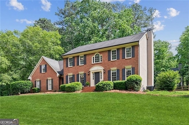 View of front of property featuring a chimney, a front yard, brick siding, and central AC