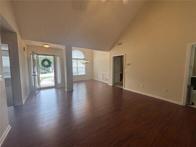 Unfurnished living room with a chandelier, dark wood finished floors, high vaulted ceiling, and baseboards