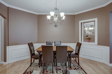 Dining space featuring a chandelier, light wood finished floors, ornamental molding, wainscoting, and a decorative wall