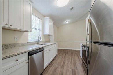 Kitchen featuring stainless steel appliances, a sink, wood finished floors, white cabinets, and baseboards
