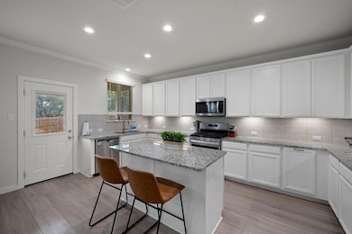 Kitchen featuring ornamental molding, stainless steel appliances, a center island, a sink, and light wood finished floors