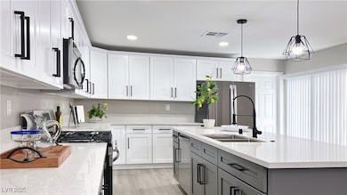 Kitchen with white cabinets, gray cabinets, an island with sink, decorative light fixtures, and appliances with stainless steel finishes