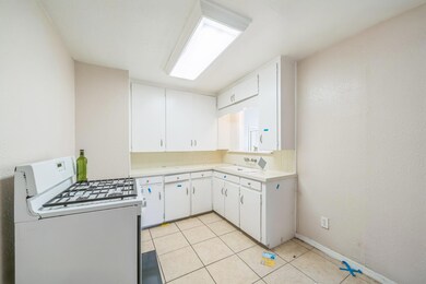 Kitchen featuring backsplash, white gas range, sink, light tile patterned floors, and white cabinets