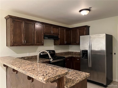 Kitchen featuring appliances with stainless steel finishes, dark stone countertops, kitchen peninsula, a breakfast bar area, and dark brown cabinetry