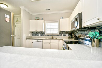 Kitchen with stainless steel appliances, backsplash, light countertops, white cabinetry, and crown molding
