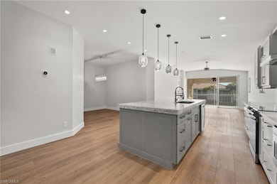 Kitchen with gray cabinetry, appliances with stainless steel finishes, a ceiling fan, a kitchen island with sink, and light wood-style flooring