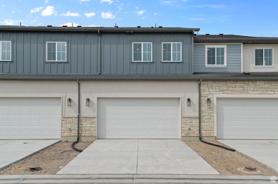 Multi unit property featuring a garage, board and batten siding, driveway, and stone siding
