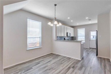Kitchen with hanging light fixtures, light stone countertops, white cabinetry, a peninsula, and light wood-type flooring