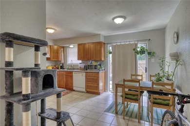 Kitchen featuring a textured wall, brown cabinets, light tile patterned flooring, light countertops, and dishwasher