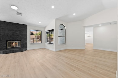 Unfurnished living room featuring recessed lighting, lofted ceiling, a large fireplace, light wood-style floors, and a textured ceiling