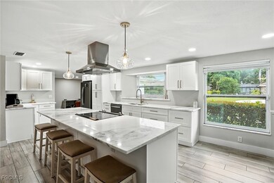 Kitchen featuring island exhaust hood, wood finish floors, light stone countertops, a kitchen breakfast bar, and white cabinetry