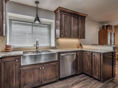 Kitchen with dishwasher, dark wood-type flooring, a peninsula, decorative backsplash, and dark brown cabinets