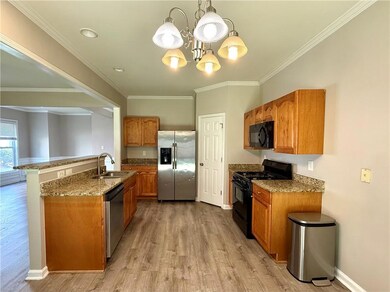 Kitchen featuring black appliances, light wood-style floors, brown cabinetry, a chandelier, and ornamental molding