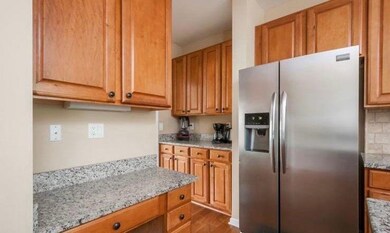 Kitchen featuring stainless steel fridge with ice dispenser, light stone counters, dark wood-style floors, brown cabinetry, and decorative backsplash