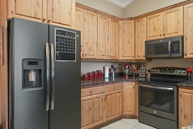Kitchen with stainless steel appliances, dark stone counters, light tile patterned flooring, ornamental molding, and light brown cabinets