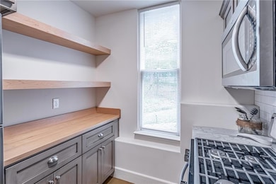 Kitchen featuring open shelves, stainless steel microwave, gray cabinets, decorative backsplash, and range with gas cooktop