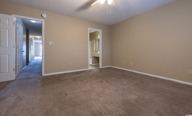 Unfurnished bedroom featuring carpet flooring, a textured ceiling, ensuite bath, and a ceiling fan
