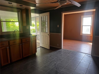 Kitchen featuring ceiling fan, a wainscoted wall, ornamental molding, brown cabinets, and wooden walls
