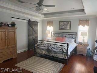 Bedroom featuring a tray ceiling, a barn door, ornamental molding, and multiple windows