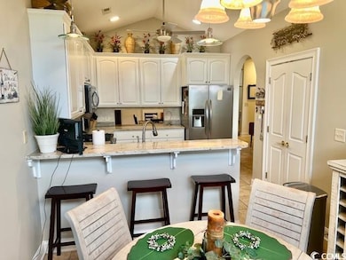 Kitchen with stainless steel appliances, a peninsula, arched walkways, white cabinetry, and a kitchen bar