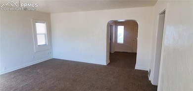 Unfurnished room with dark carpet, plenty of natural light, arched walkways, and baseboards