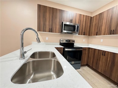 Kitchen featuring appliances with stainless steel finishes, light hardwood / wood-style flooring, sink, and light stone counters