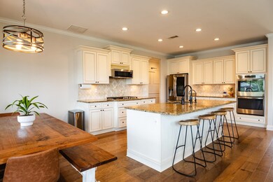 Kitchen with appliances with stainless steel finishes, light stone countertops, ornamental molding, a kitchen island with sink, and backsplash