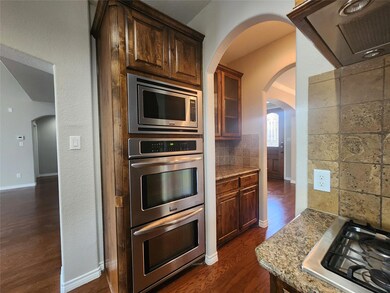 Kitchen featuring dark wood-type flooring, light stone counters, stainless steel appliances, and tasteful backsplash