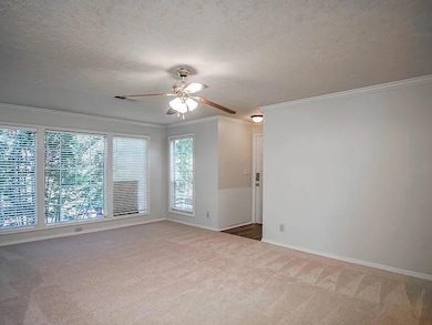 Empty room with crown molding, a textured ceiling, light colored carpet, and a ceiling fan