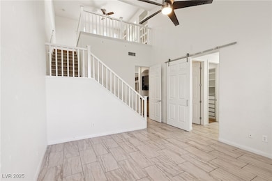 Unfurnished living room with ceiling fan, a barn door, a high ceiling, and stairway