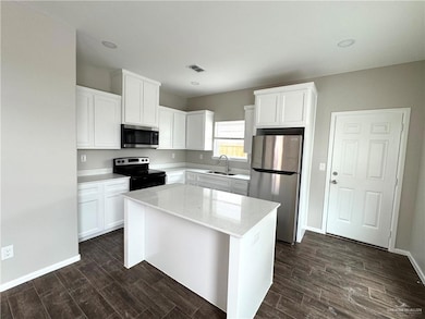 Kitchen featuring appliances with stainless steel finishes, a sink, dark wood-style floors, and a kitchen island