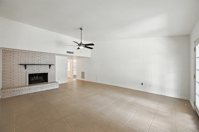 Unfurnished living room featuring a brick fireplace, light tile patterned floors, and a ceiling fan