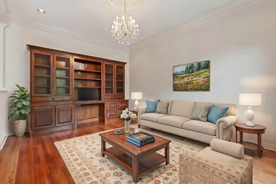 17x14 Spacious Living Room Featuring Hardwood Floors, Elegant Crown Molding, Crystal Chandelier, and a Beautiful Custom Built-In Bookcase with Desk Area — Ideal for Entertaining or a Stylish Home Office!  This photo is virtually staged.