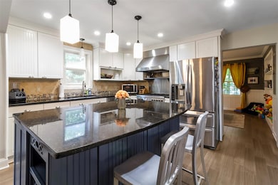 Kitchen featuring wall chimney range hood, appliances with stainless steel finishes, open shelves, a kitchen island, and white cabinets