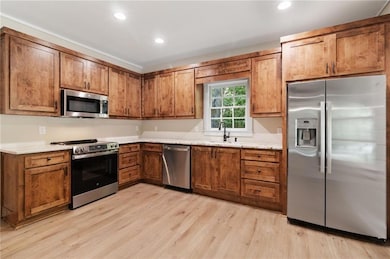 Kitchen with appliances with stainless steel finishes, brown cabinetry, light wood-type flooring, recessed lighting, and light stone counters