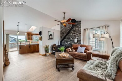 Living room featuring a wood stove, healthy amount of natural light, light wood finished floors, a ceiling fan, and high vaulted ceiling