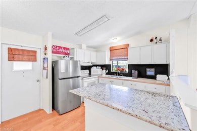 Kitchen featuring light wood-type flooring, a sink, under cabinet range hood, white appliances, and white cabinets