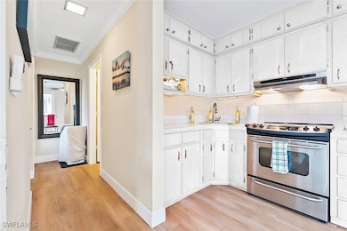 Kitchen featuring ornamental molding, sink, white cabinetry, stainless steel electric stove, and light wood-type flooring