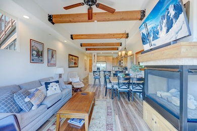 Living room featuring beamed ceiling, light wood-style flooring, recessed lighting, a ceiling fan, and a chandelier