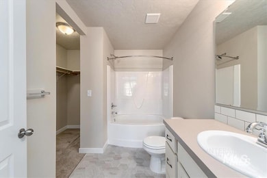 Full bathroom with a textured ceiling, vanity, shower / bath combination, a walk in closet, and light tile patterned floors