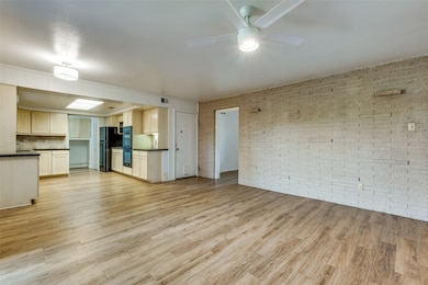 Unfurnished living room featuring light wood-style floors, brick wall, and a ceiling fan