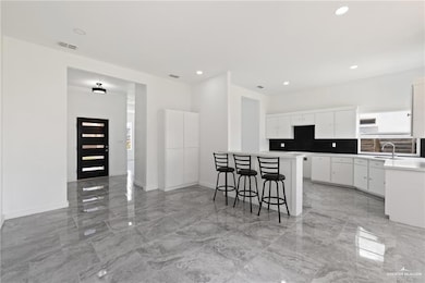 Kitchen featuring a kitchen breakfast bar, white cabinetry, light marble finish floors, light countertops, and backsplash
