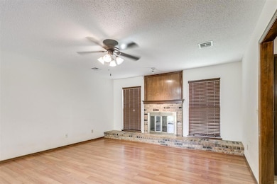Unfurnished living room featuring a ceiling fan, light wood-style flooring, a textured ceiling, and a fireplace