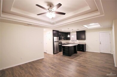 Kitchen with a raised ceiling, a center island, hanging light fixtures, stainless steel appliances, and dark wood-type flooring