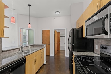 Kitchen featuring electric stove, light brown cabinetry, light stone counters, stainless steel microwave, and concrete floors