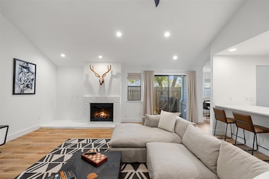 Living room with recessed lighting, light wood-type flooring, a warm lit fireplace, and lofted ceiling