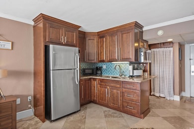 Kitchen featuring freestanding refrigerator, light stone counters, backsplash, ornamental molding, and black microwave