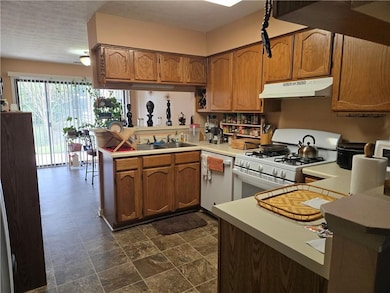 Kitchen featuring white appliances, light countertops, brown cabinetry, a peninsula, and under cabinet range hood